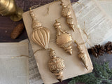 Six gold baubles made with I.O.D. 2026 Baubles Mould displayed on a book with old paper, pinecones, and greenery.