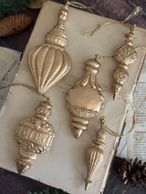 Five I.O.D. Baubles Mould (2026 Limited Release) ornaments on a vintage book with pinecones and gold strings.