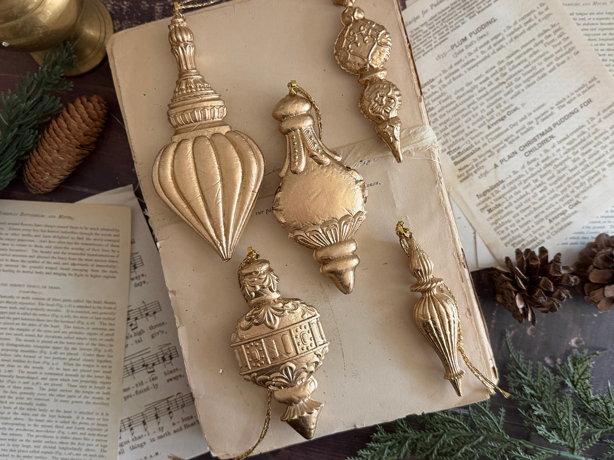 Five Baubles Mould (2026 Limited Release) ornaments by I.O.D. displayed on a book with pine cones and greenery.