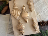 Six Baubles Moulds by I.O.D. arranged on a book with visible sheet music and pinecones.