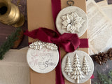 Three I.O.D. Boughs of Holly (2026 Limited Release) ornaments on a gift box with red ribbon and book pages.