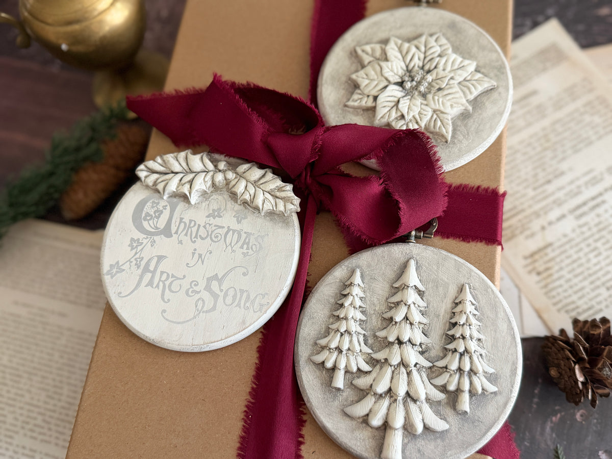 Brown paper-wrapped gift with red ribbon, adorned with I.O.D. Boughs of Holly (2026 Limited Release) ornaments.
