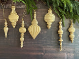 Seven gold ornate Baubles Moulds (2026 Limited Release) by I.O.D. displayed beneath pine on a dark wooden surface.