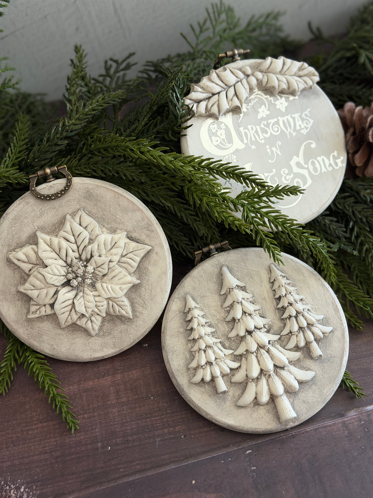 Boughs of Holly (2026) by I.O.D.; 3 round beige ornaments with vintage moulds—poinsettia, trees, festive text.