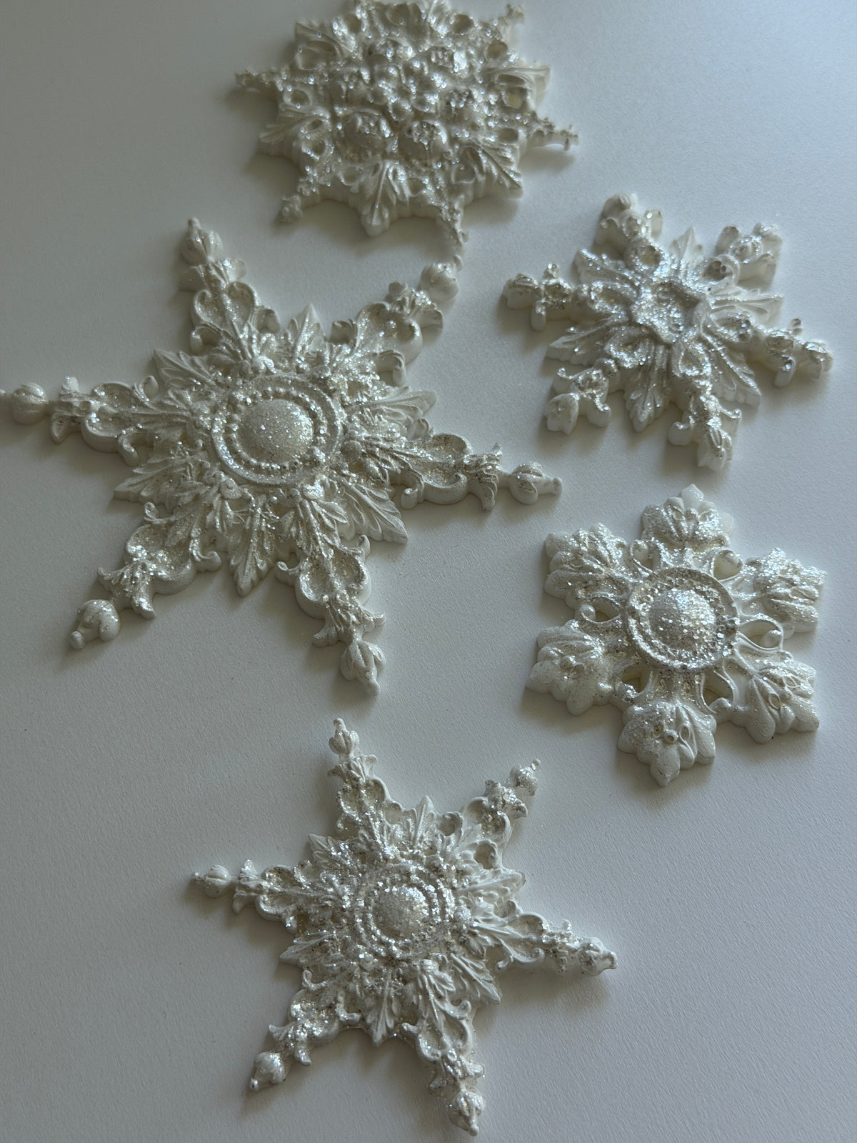 Five white ornaments made with I.O.D. Snowflakes Mould (2026 Limited Release) displayed on a plain surface.