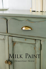 Green cabinet in Acadia Pear Milk Paint by Homestead House with brass handles, shown in close-up.