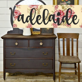 Dresser painted with Adelaide by Old Fashioned Milk Paint, next to a wood chair and floral sign on shiplap wall.