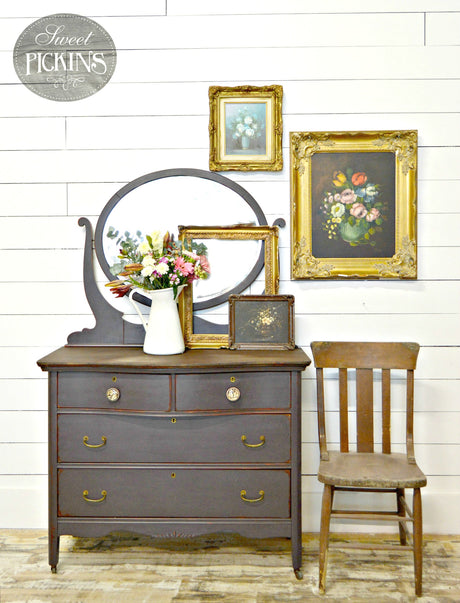 Gray vintage dresser with mirror, painted in Adelaide by Old Fashioned Milk Paint; includes wooden chair and floral wall art.
