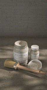 Jar, small bottle, Alabaster Alchemy Paint by Fusion Mineral Paint, and brush arranged on a textured surface.