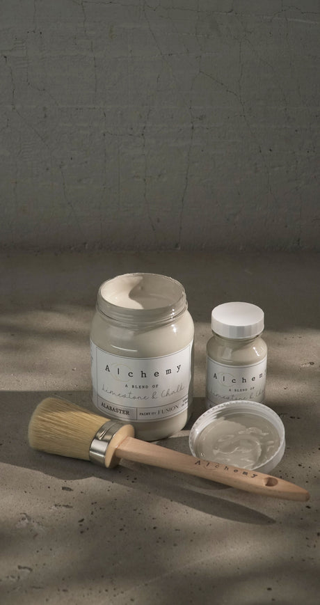 Jar, small bottle, Alabaster Alchemy Paint by Fusion Mineral Paint, and brush arranged on a textured surface.