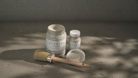 Three jars of Alabaster Alchemy Paint by Fusion with a wooden brush on concrete.