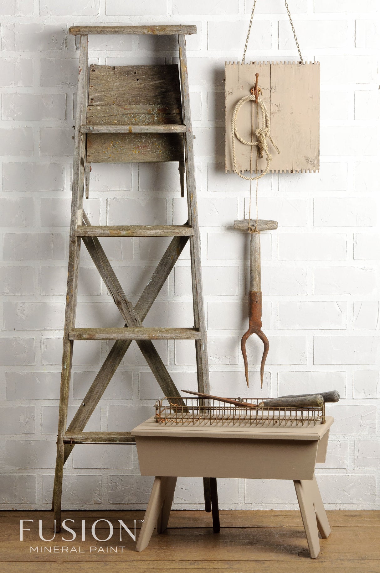 Rustic wooden ladder painted Algonquin by Fusion Mineral Paint beside beige stool against white brick wall.
