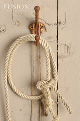 Rusted hook with coiled rope on a weathered Algonquin by Fusion Mineral Paint wall; logo in corner.