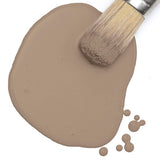 Paintbrush on spilled Fusion Almond Latte Milk Paint with visible droplets nearby.