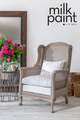 Beige armchair with white cushion beside table, pink flowers, and baskets; Fusion Mineral Paint Almond Latte above.
