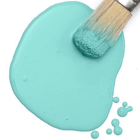 Paintbrush on a puddle of Amalfi Coast Milk Paint by Fusion Mineral Paint, with scattered drops on a white background.