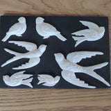 Seven white bird figures made with Notions Amazing Casting Resin using IOD Decor Moulds, displayed on black background.