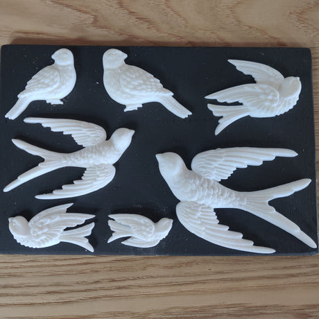 Seven white bird figures made with Notions Amazing Casting Resin using IOD Decor Moulds, displayed on black background.