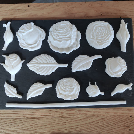 White rose, leaf, and bud shapes cast with Amazing Casting Resin (White) by Notions on a black background.