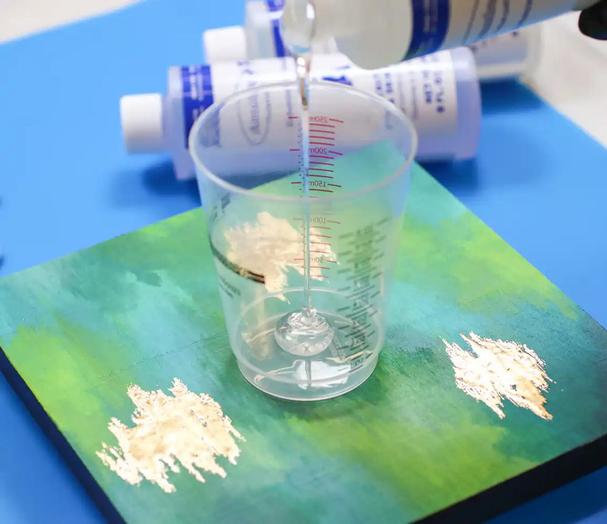 Amazing Clear Cast +Plus Epoxy by Notions being poured into a cup, with product bottles visible in the background.