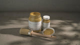 Two jars of Fusion Mineral Paint Amber Alchemy, one open, with a paintbrush beside them.