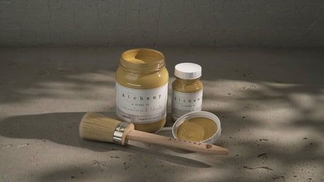 Two jars of Fusion Mineral Paint Amber Alchemy, one open, with a paintbrush beside them.
