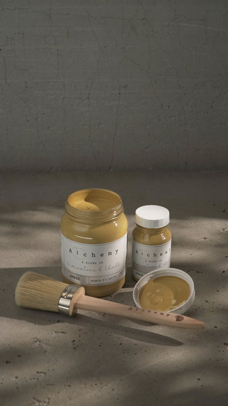 Fusion Amber Alchemy Paint jar with lid and a paintbrush on a gray surface.