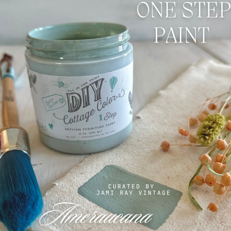 Open jar of Ameraucana DIY Cottage Color by DIY Paint Co. with brush, paint swatch, and dried flowers nearby.
