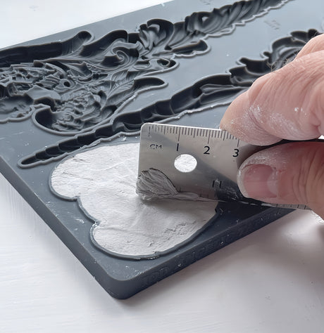 Hand spreading plaster into I.O.D. Angelic Tapers Mould (2024) with a marked metal scraper.