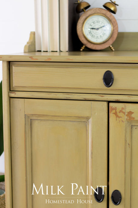 Yellow distressed cabinet with black handles, books, and a vintage clock. Antique Gold Milk Paint by Homestead House.