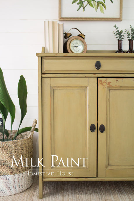 Sideboard in Antique Gold Milk Paint by Homestead House, displayed with books, a clock, and plants on top.