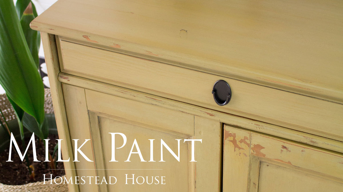 Yellow cabinet with chipped finish, black knob, and Antique Gold Milk Paint by Homestead House text in front.