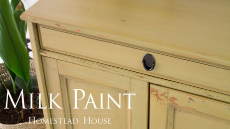 Yellow cabinet with chipped finish, black knob, and Antique Gold Milk Paint by Homestead House text in front.