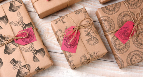 Four brown paper-wrapped gifts with I.O.D. Antiquities Stamps and red tags on a light wood surface.