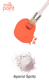 Paintbrush with orange paint, powder, and Fusion Mineral Paint Aperol Spritz Milk Paint on white background.