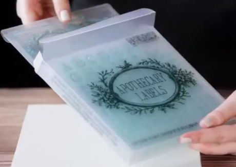Hands holding I.O.D. Apothecary Mini-Stamp by Iron Orchid Designs against a light background.