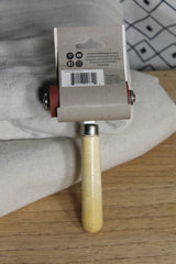I.O.D. Art Brayer with handle and tag shown on white cloth over wood.