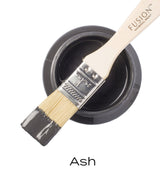Open can of Ash Fusion Mineral Paint with brush dipped in dark charcoal grey acrylic paint.