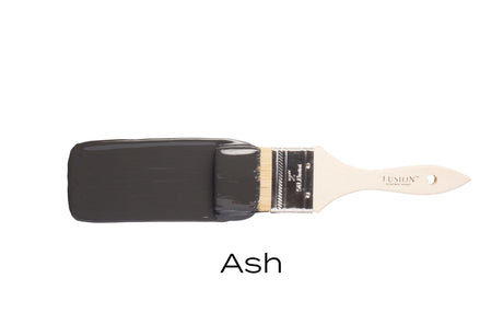 Paintbrush dipped in Fusion Mineral Paint Ash, a dark charcoal grey acrylic, on plain white background.