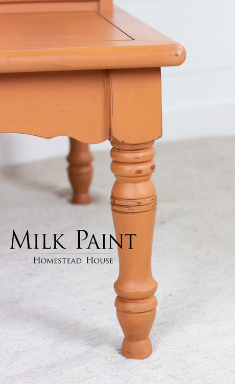 Orange-painted wooden table leg with visible Homestead House Autumn Leaves Milk Paint label in black lettering.