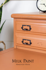 Orange wooden desk with black metal handles, clock on top; finished in Autumn Leaves Milk Paint by Homestead House.