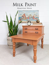 Vintage side table in Homestead House Autumn Leaves Milk Paint with drawers, topped with a plant, books, and clock.