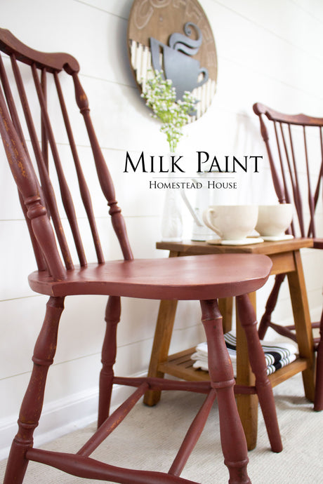 Two Barn Red Milk Paint chairs by Homestead House next to a table holding mugs, flowers, and art.