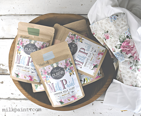 Four bags of Basil Sweet Pickins Milk Paint by Old Fashioned Milk Paint with floral fabric and logo nearby.