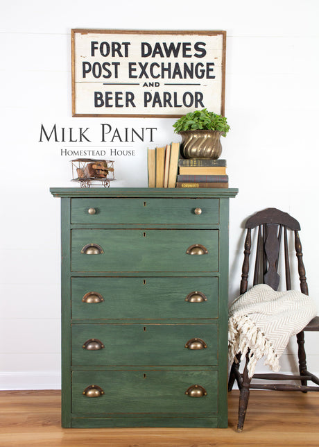Green dresser painted in Homestead House Bayberry Milk Paint with brass handles, books, and a plant displayed on top.
