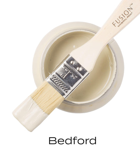 Paintbrush with beige paint resting on open jar of Fusion Mineral Paint Bedford.