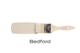 Paintbrush with Fusion Mineral Paint Bedford, a neutral grey shade, against a white background.