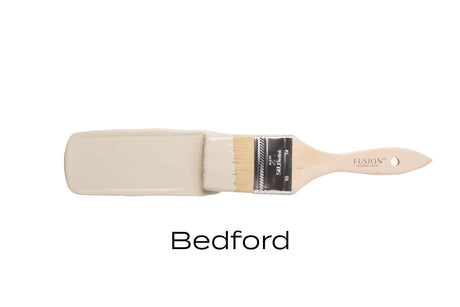 Paintbrush with Fusion Mineral Paint Bedford, a neutral grey shade, against a white background.