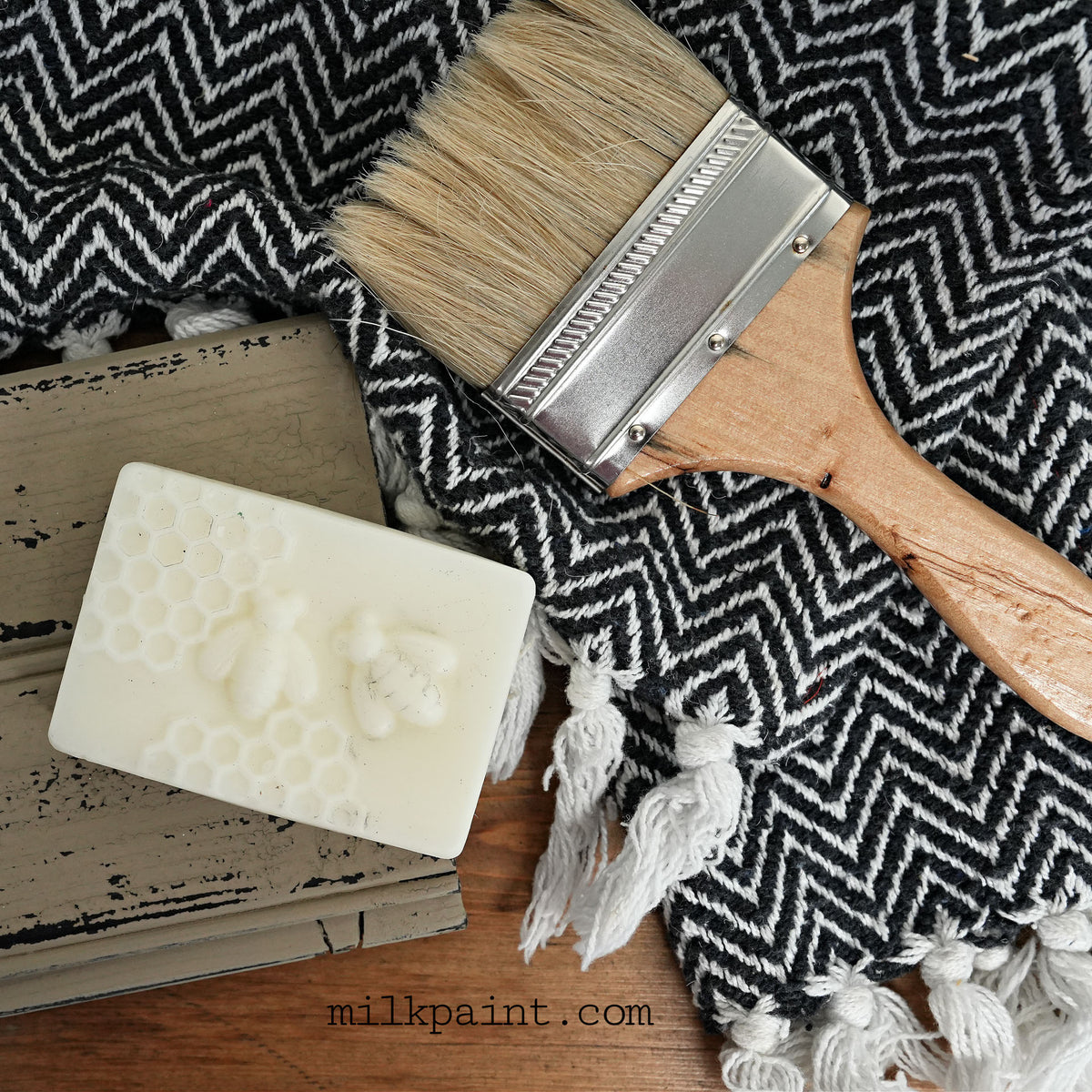 An Old Fashioned Milk Paint Beeswax Bar, brush, and cloth on wood surface for use with milk paint.