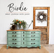 Green “Birdie” dresser by Old Fashioned Milk Paint, shown near flowers and a rustic door with a wreath.